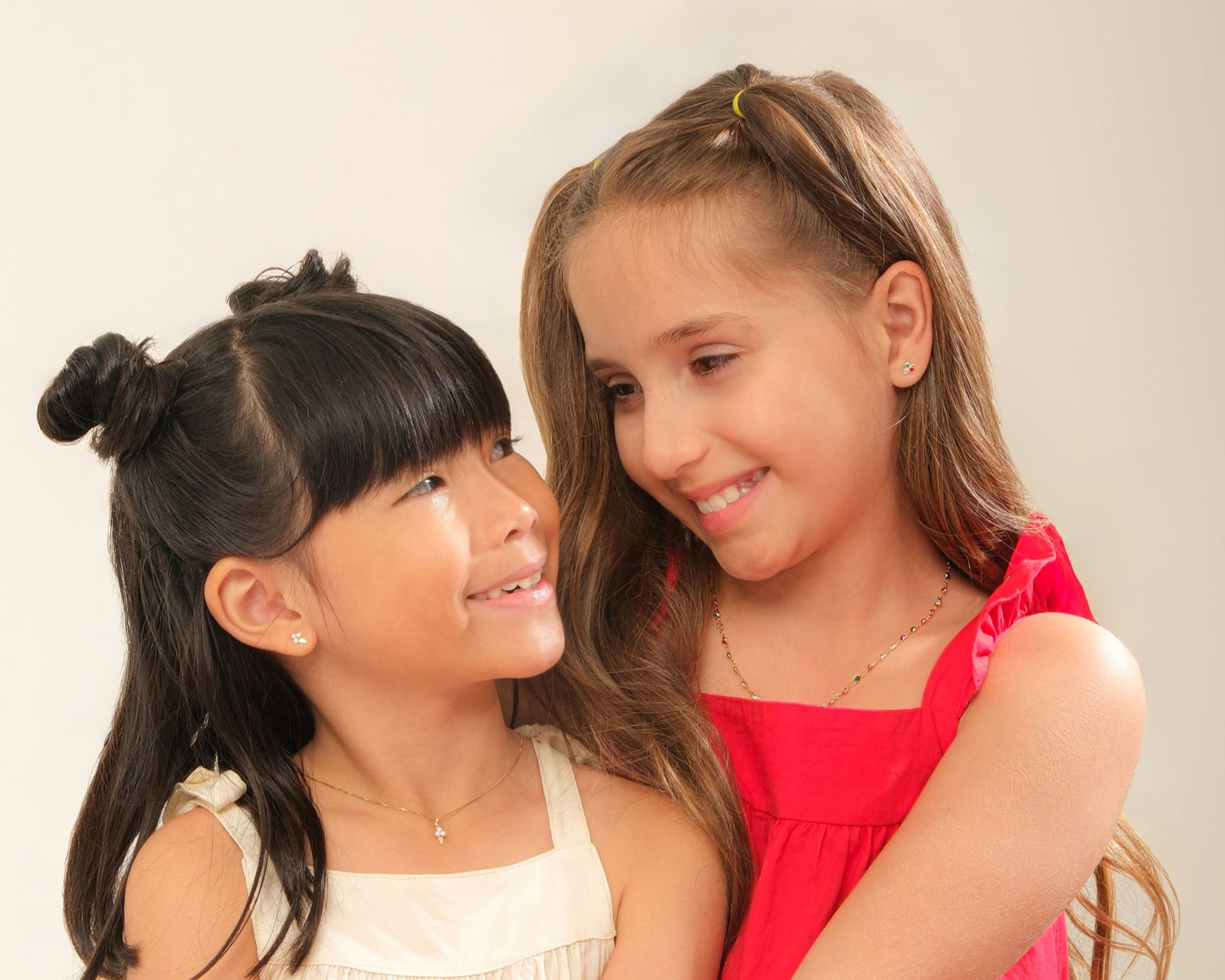 Two young girls hugging each other against a plain background